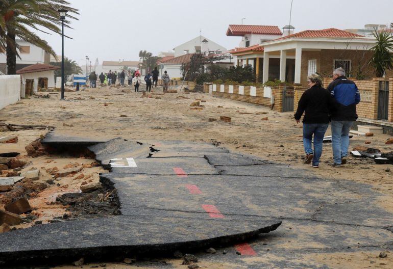 Vecinos de La Antilla (Huelva), una de las zonas más castigadas por el temporal, caminando por una calle destrozada de este núcleo urbano. Se ha prohibido la entrada a 30 viviendas por precaución. 