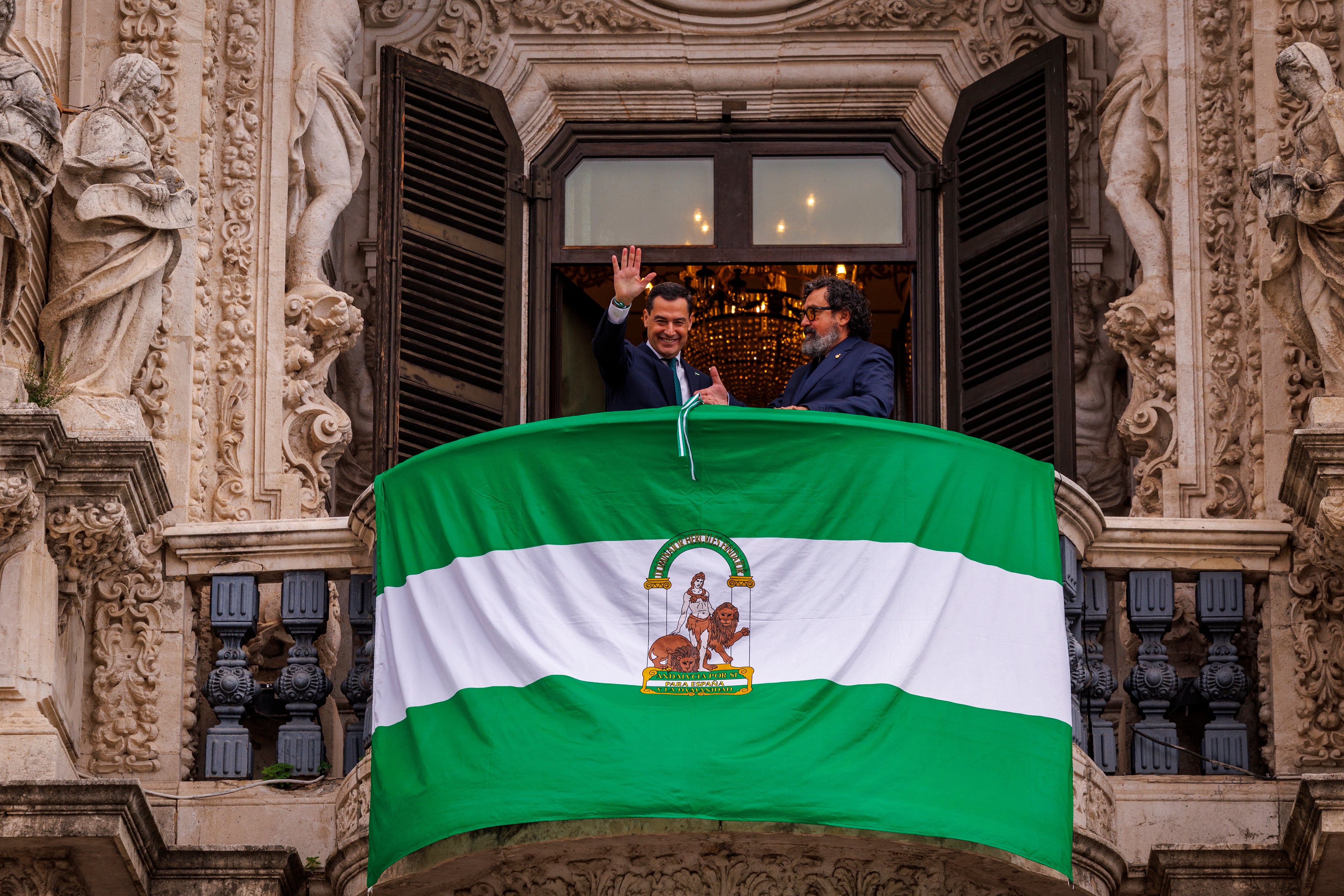 GRAFAND5336.-  SEVILLA, 04/12/2024.- El presidente andaluz, Juanma Moreno, y el actor Paco Tous (d), tras desplegar una bandera de Andalucía en el balcón del Palacio de San Telmo o, sede del ejecutivo autónomo en Sevilla para celebrar el Día de la Bandera, que recuerda las masivas manifestaciones que tuvieron lugar el 4 de diciembre de 1977 reclamando la autonomía. EFE/ Julio Muñoz
