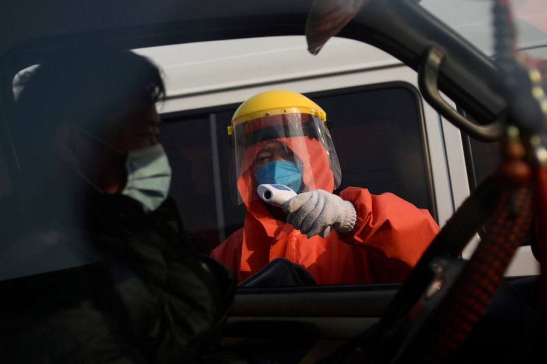 Un trabajador compreba la temperatura de un hombre desde el interior de su vehículo en las instalaciones del mercado de Xinfadi, en Pekín (China).