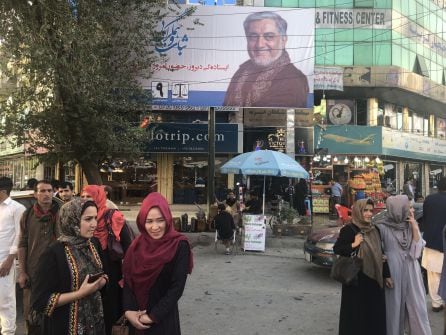 Kabulíes esperan transporte ante un cartel electoral