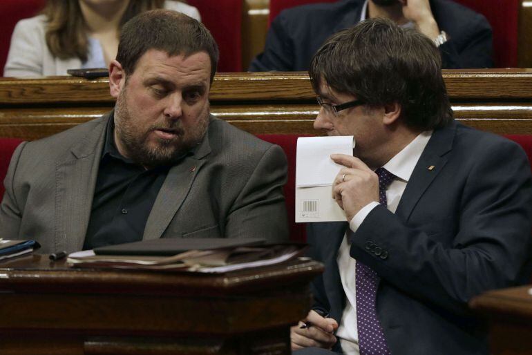 El presidente de la Generalitat, Carles Puigdemont (d) conversa con el vicepresidente Oriol Junqueras (i) , durante la primera sesión de control al nuevo gobierno catalán que se celebra en el Parlament de Cataluña