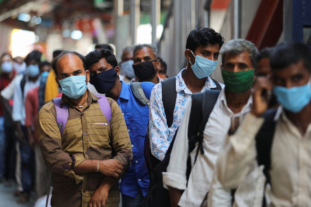 Un grupo de pasajeros con mascarilla espera abordar un tren en una estación de Nueva Delhi (India).