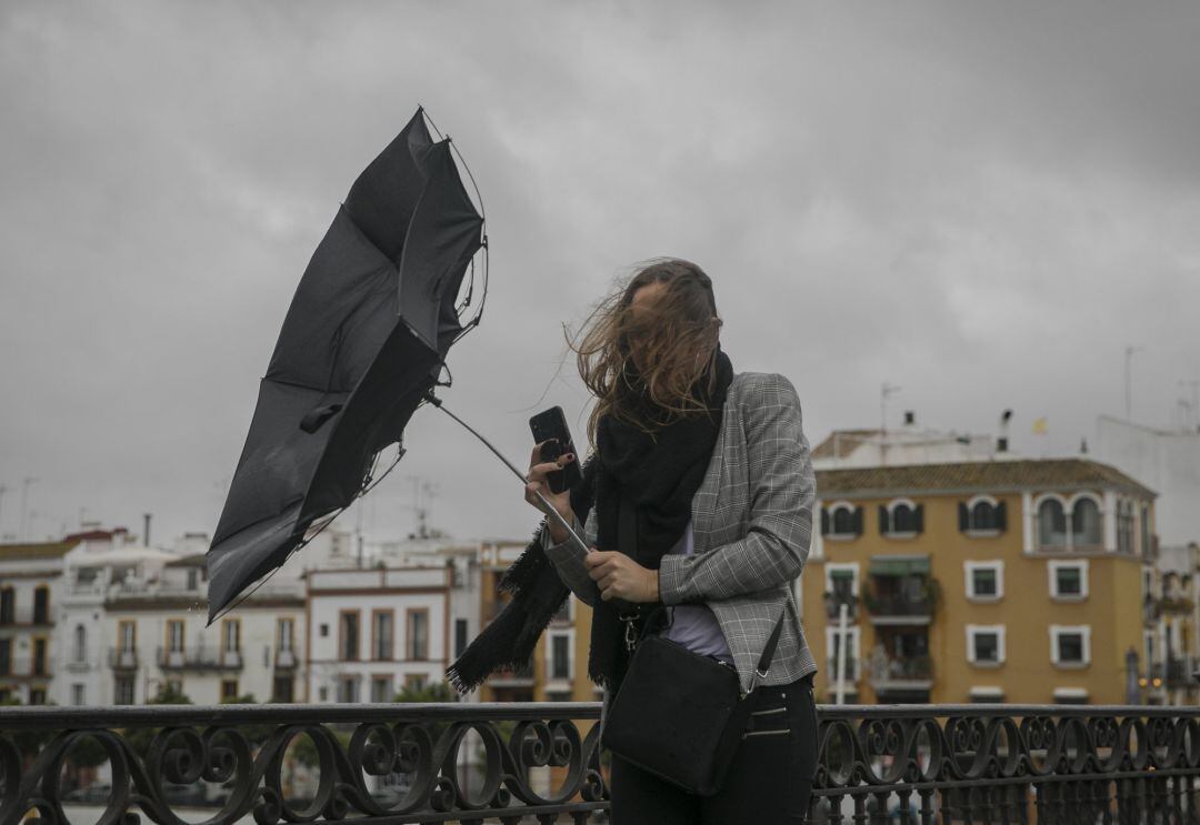 Una racha de viento desbarata el paragüas de una viandante mientras camina por el Puente de Isabel II, en Sevilla