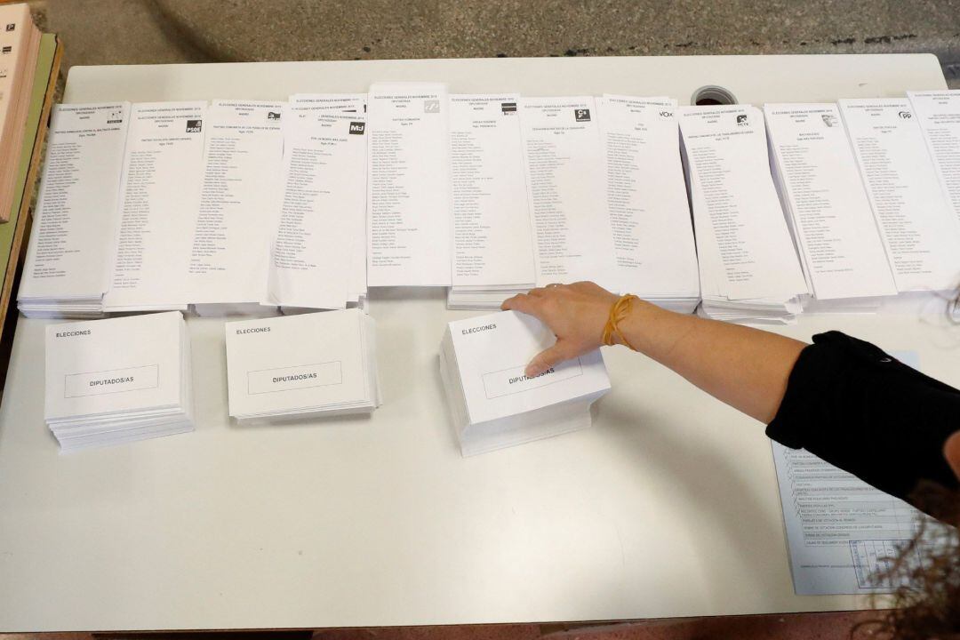 Una persona coloca las listas con las diferentes candidaturas que concurren a las elecciones generales en el montaje del colegio electoral en el CEIP Pi i Margall de Madrid