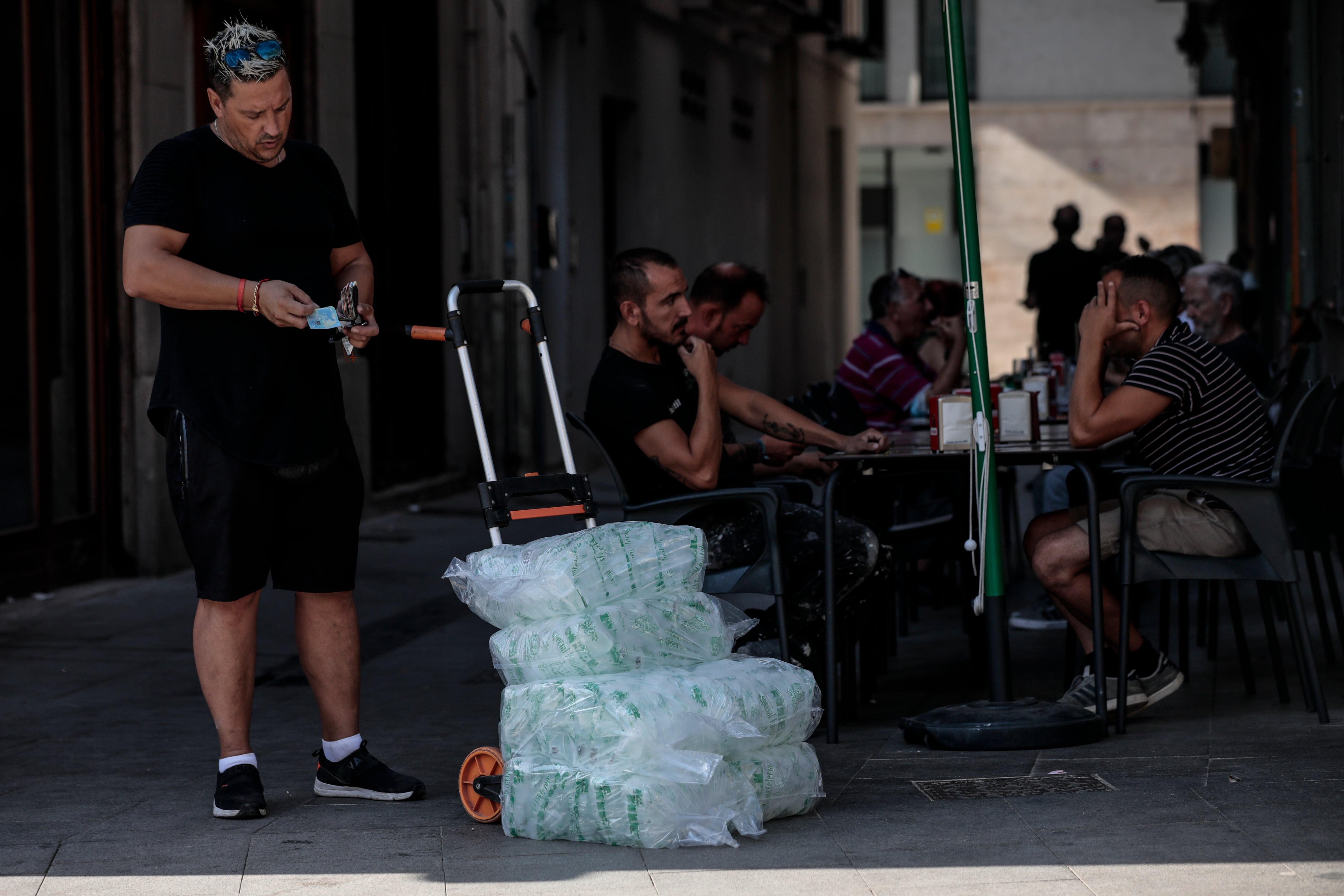 Un repartidor lleva una carretilla cargada con bolsas de hielo a un bar en Valéncia