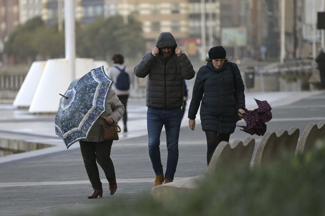 Tres personas con paraguas en el Paseo Marítimo de A Coruña donde se aprecia fuerte viento como consecuencia de la borrasca Barra, este martes.