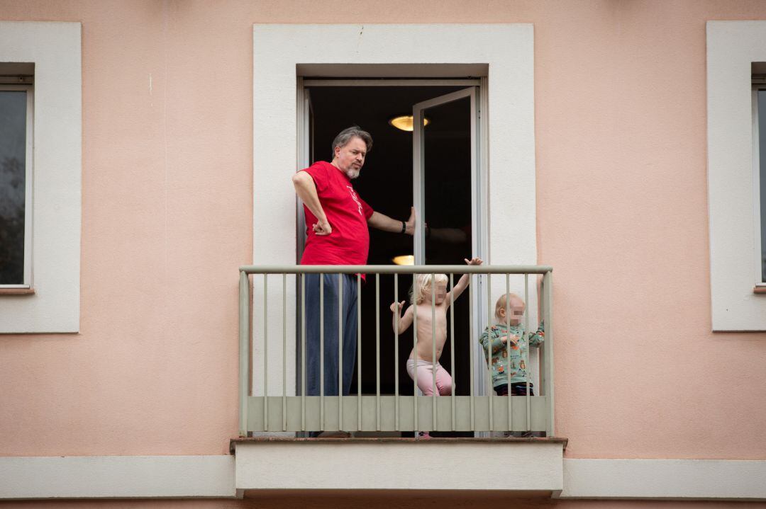 Un hombre y sus dos hijos pequeños se asoman al balcón el pasado martes en Barcelona.