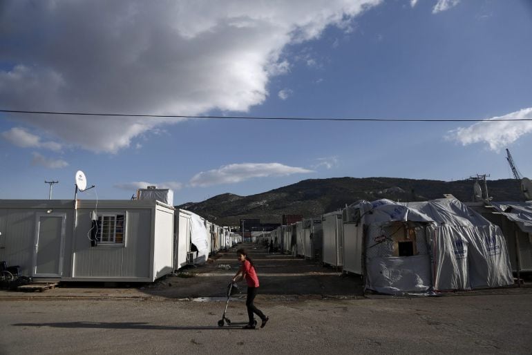 YA01 ATENAS (GRECIA) 13 12 2016.- Una niña refugiada monta en su patinete en frente de los contenedores utilizados como casas temporales en el campamento de refugiados de Skaramangas, cerca de Atenas, Grecia, hoy, 13 de diciembre de 2016. Cerca de 60.000 