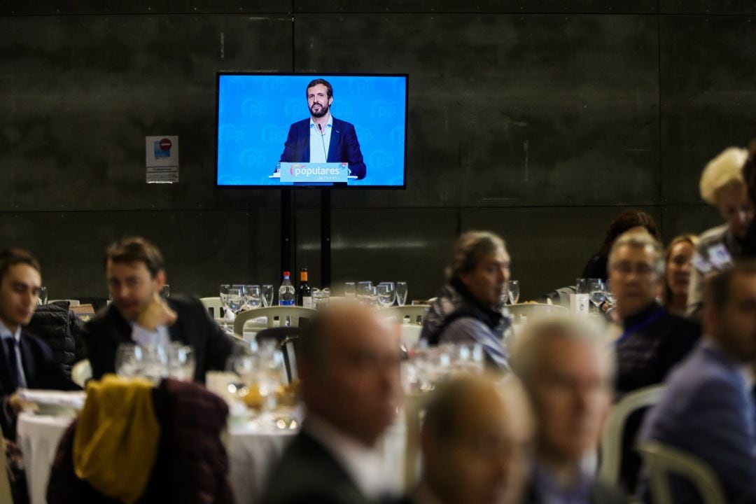 El presidente nacional del PP, Pablo Casado, en la pantalla, en la tradicional comida de Navidad del PP de la Comunidad de Madrid