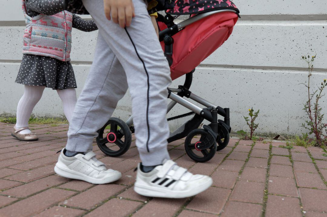 Una niña pasea por la calle empujando un carrito con un bebé