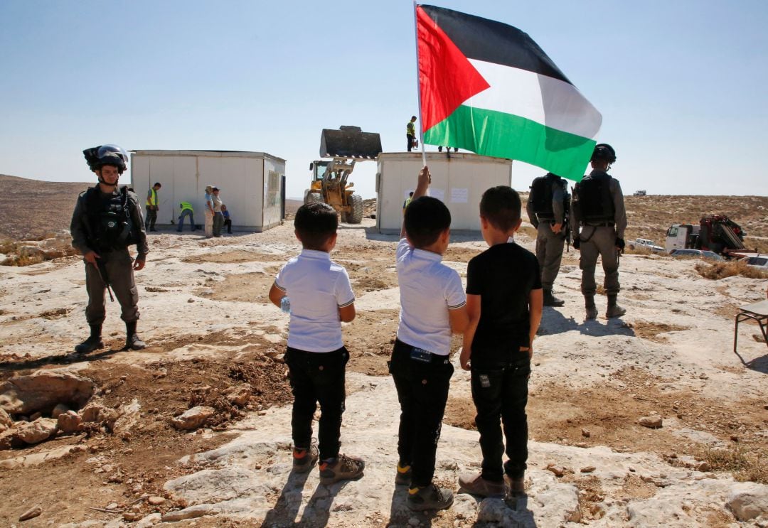 Unos niños sostienen la bandera palestina mientras son evacuados después de que su escuela haya sido demolida en Yatta