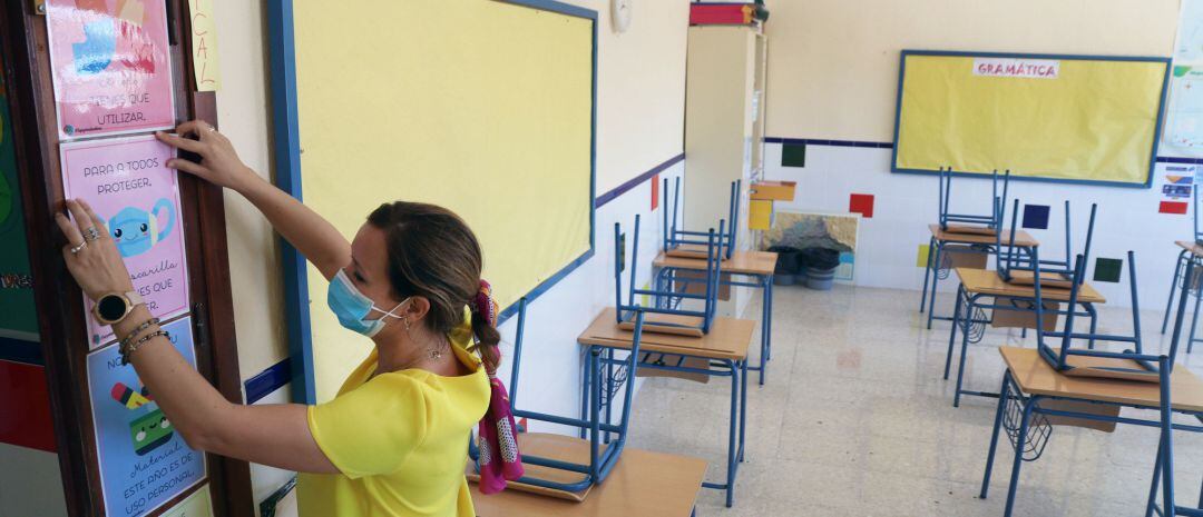 Una profesora coloca carteles de medidas preventivas ante el COVID-19 en el aula antes del inicio del curso escolar en un colegio.