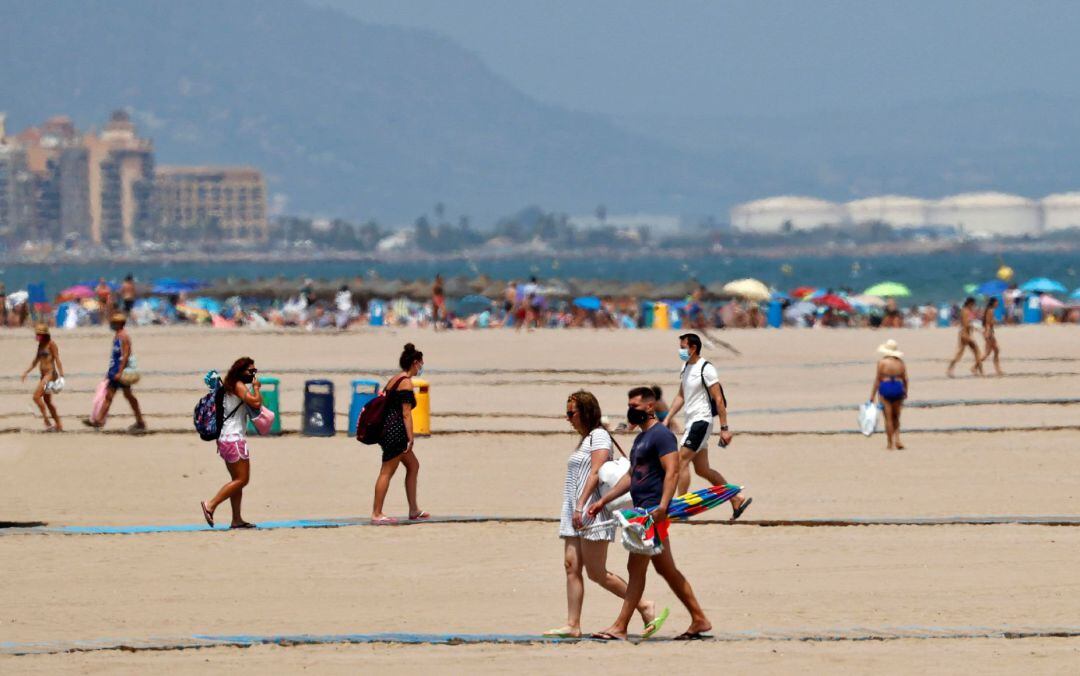 Varias personas caminan hacia y desde la orilla de la playa de la Malvarrosa de Valéncia