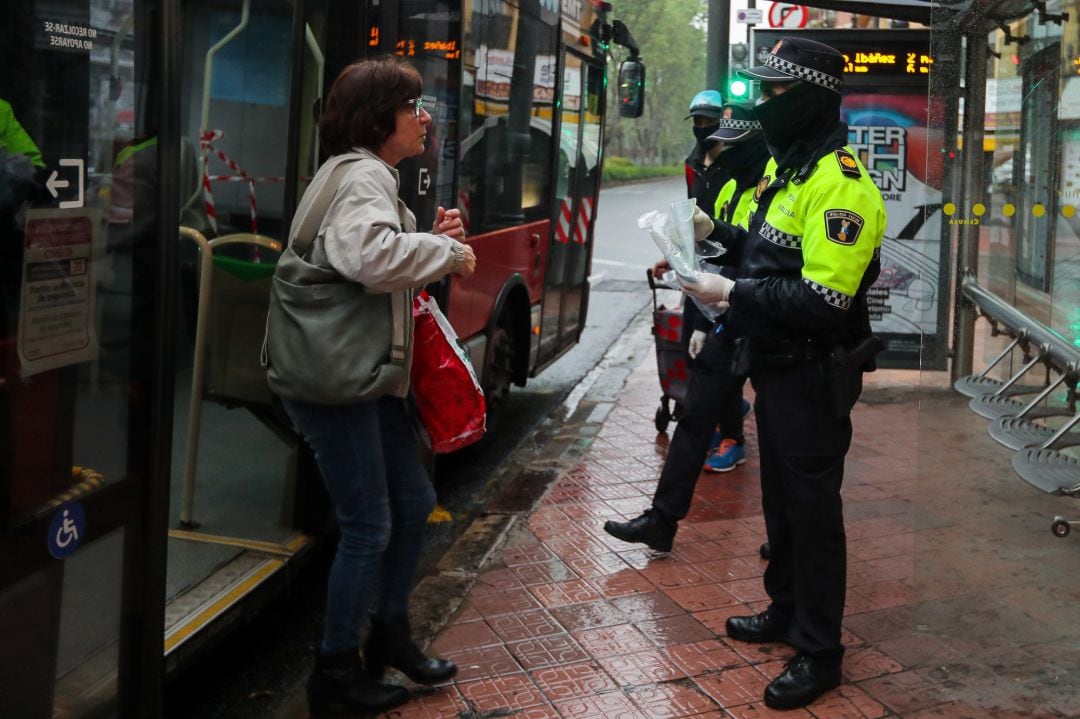 Un agente de policía local de Valencia entrega mascarillas a usuarios de autobuses urbanos de Valencia