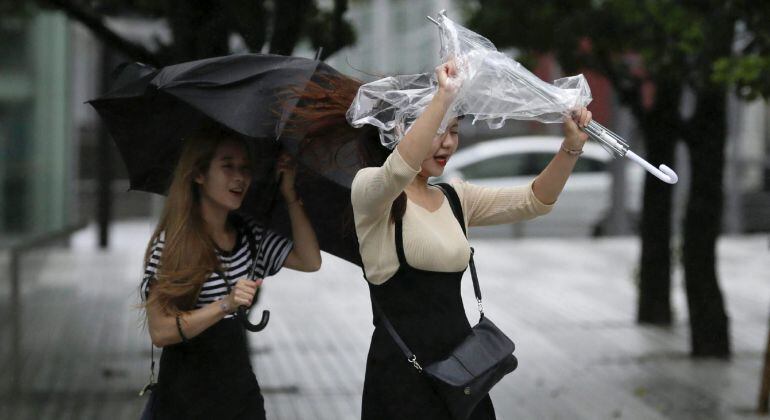 Dos mujeres agarran sus paraguas contra la lluvia y el fuerte viento mientras el tifón Mindulle que golpea el este de Japón llega a Tokio.