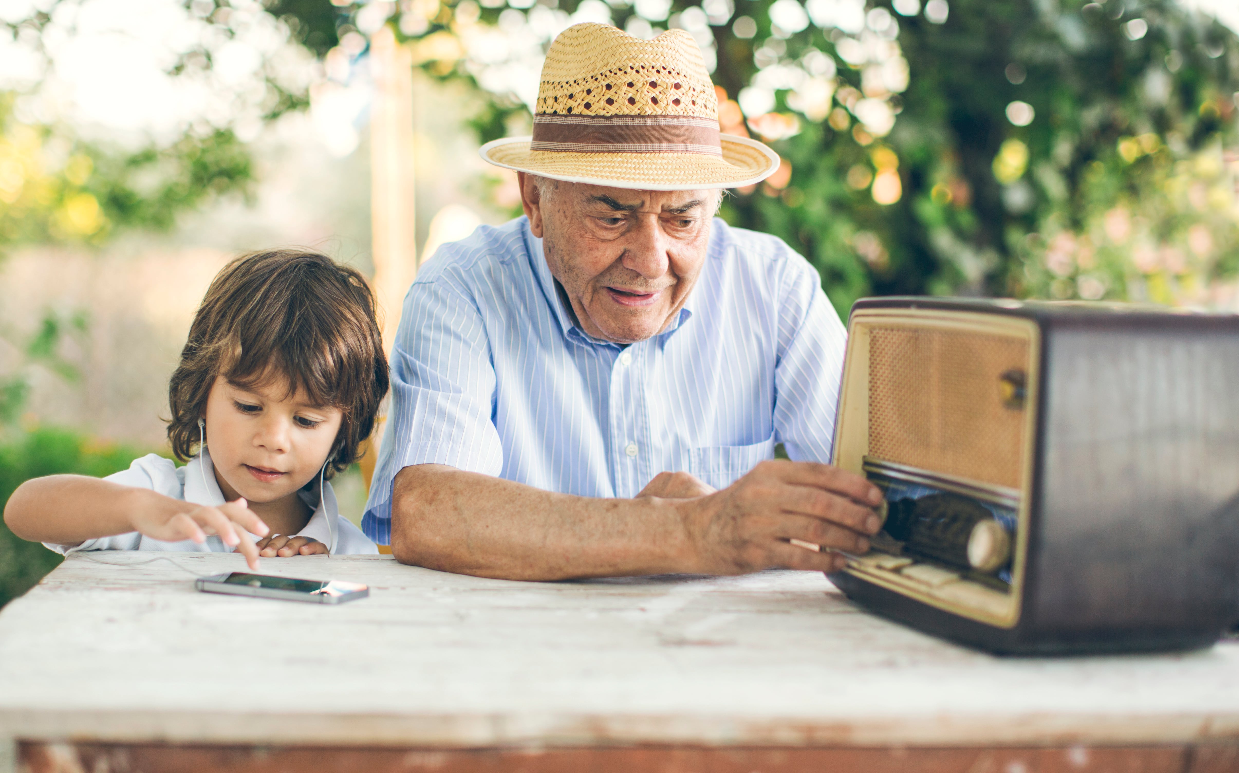 Small kid listening music from a smart phone while his grandfather from an old radio