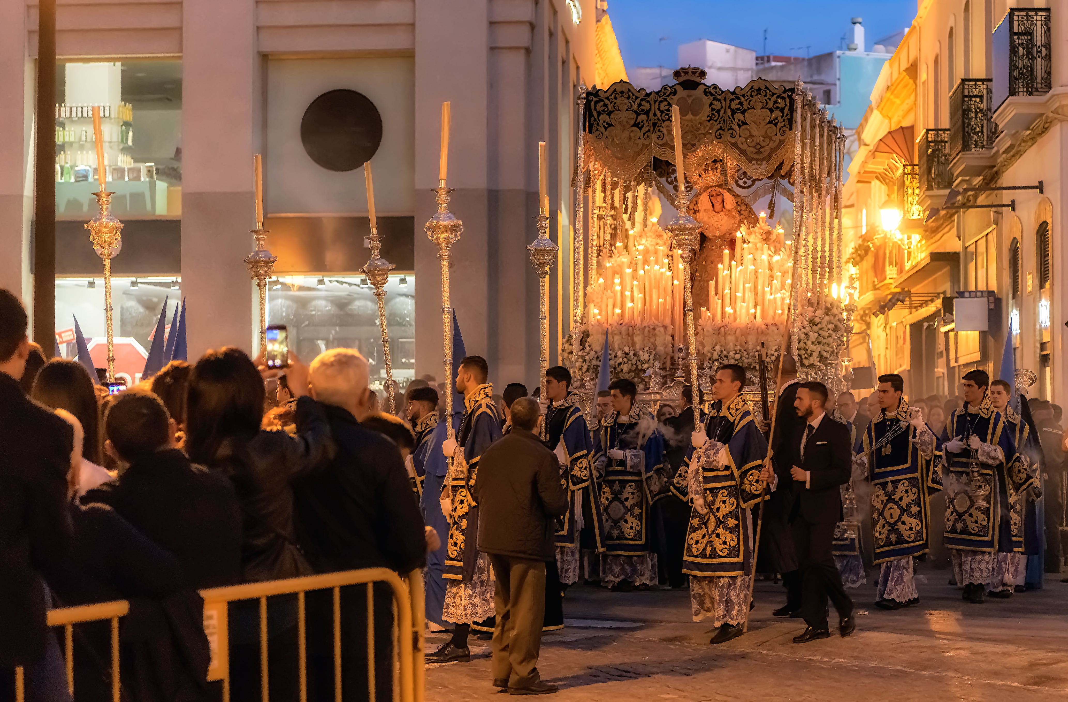 Candles illuminate a sculpture depicting virgin Mary on a religious float during Holy Week procession in Huelva at night.