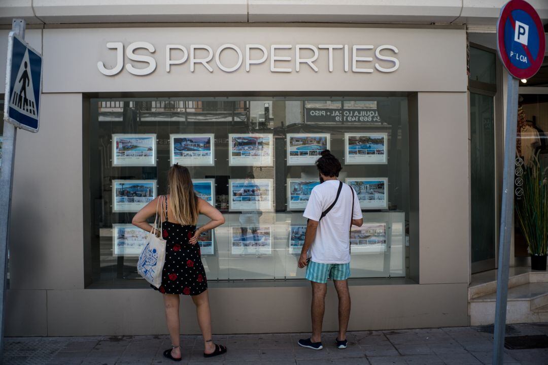 Archivo - Dos personas observan inmuebles en alquiler y en venta en un escaparate de una inmobiliaria ubicada en Palma.