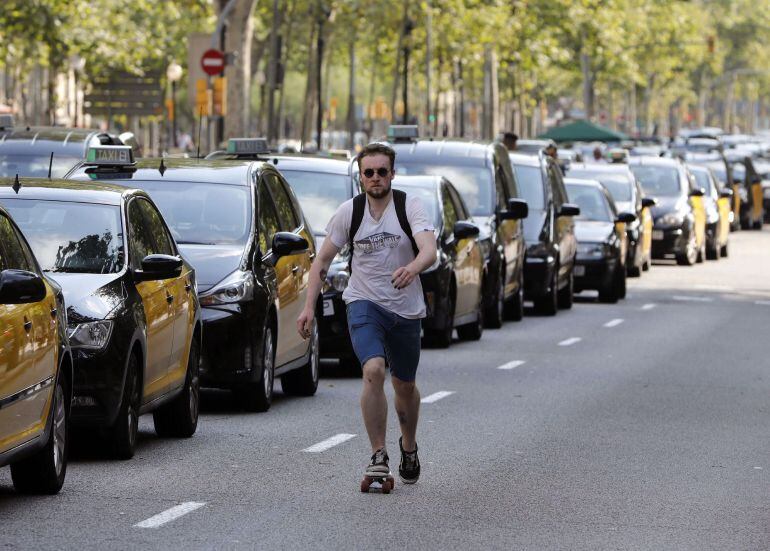 Un joven pasa ante los taxis que ocupan la Gran Vía de Barcelona durante la huelga indefinida de taxistas