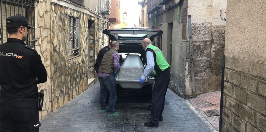 Tres personas trasladan el cadáver de la persona asesinada el pasado mes de mayo en la calle Clavario de la capital.