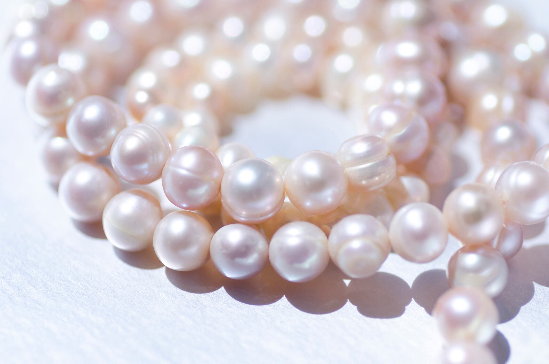 Close-up of a pink-colored pearl necklace, coiled around itself on a silver background.