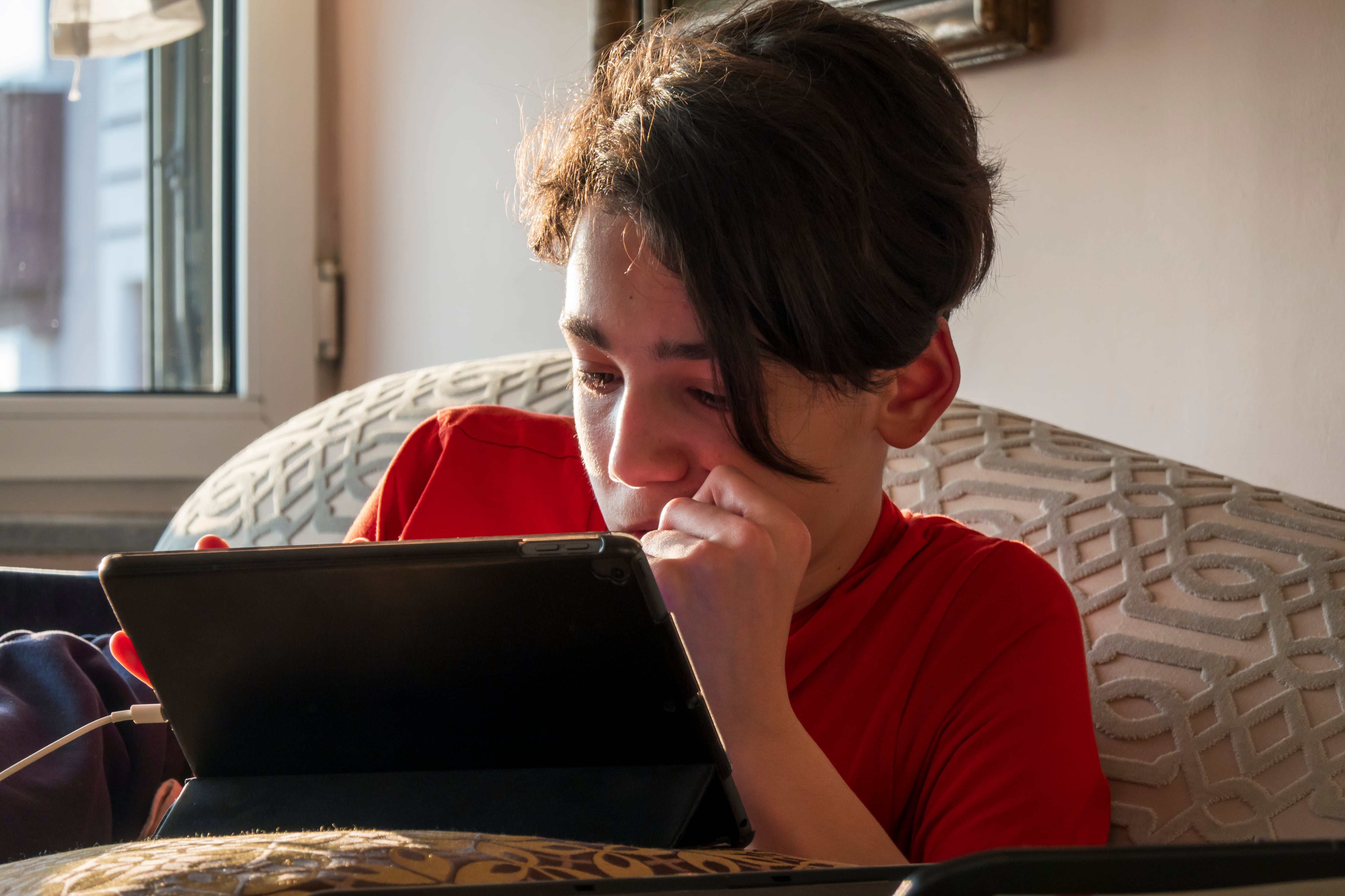 Un joven juega con una tablet en el sofá de su casa