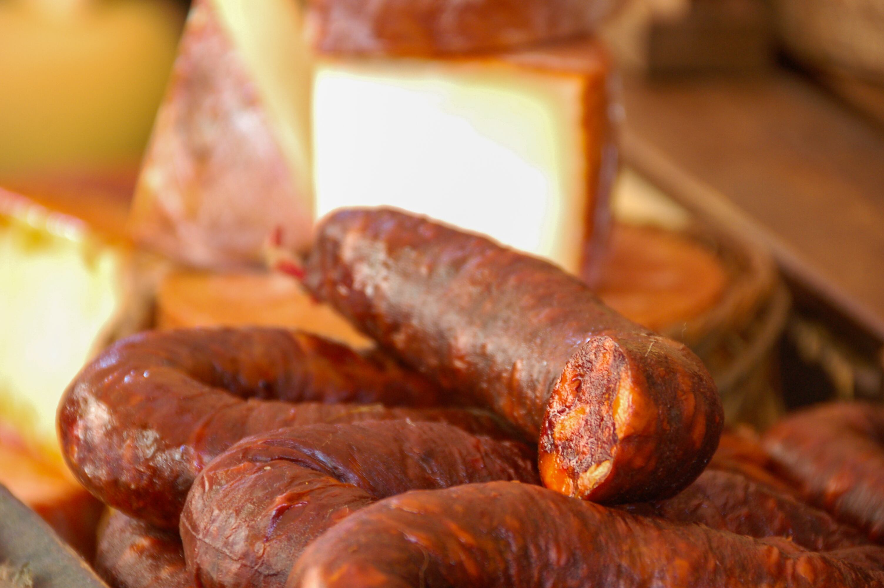 Chorizos ibéricos dispuestos sobre un plato en primer plano, con quesos al fondo sobre una tabla