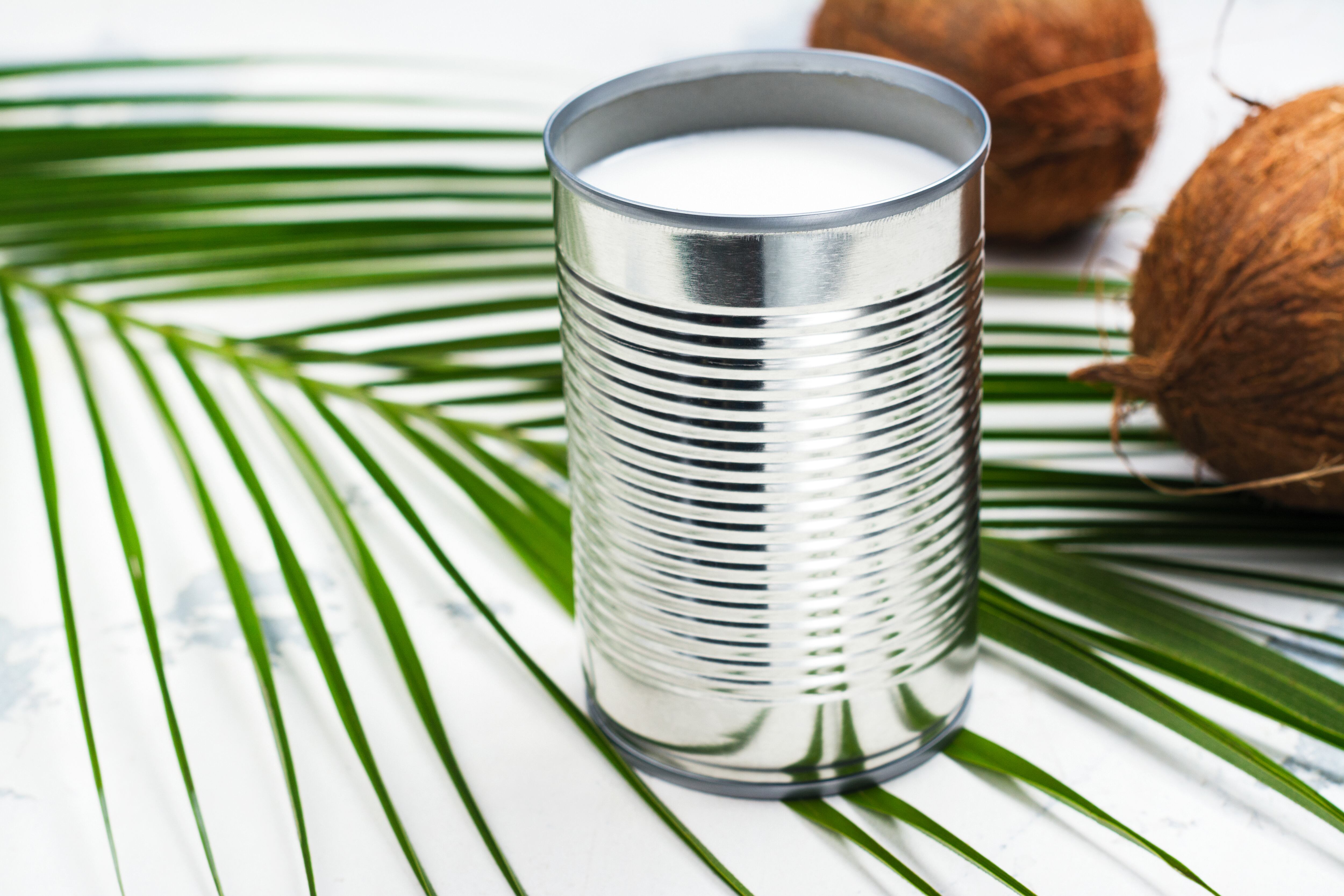 Opened tin can with coconut milk drink. Alternative non dairy vegan milk on white stone table