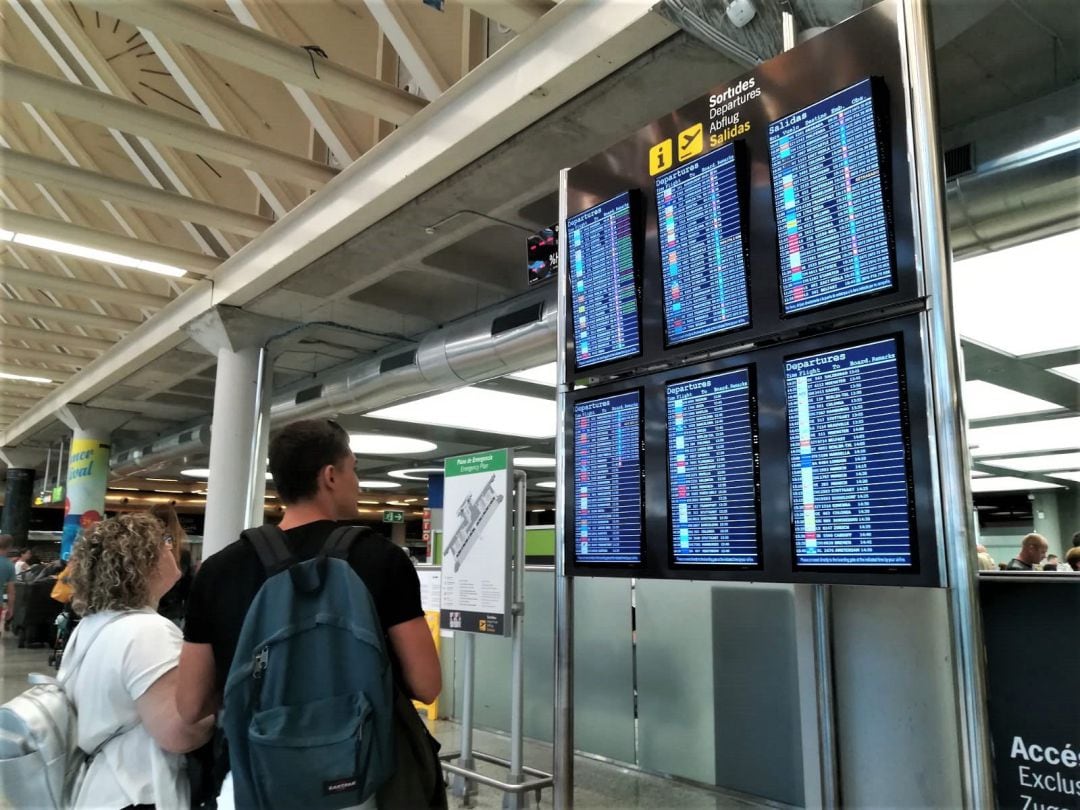 Dos viajeros consultan la información de vuelos en las pantallas del aeropuerto de Barajas.