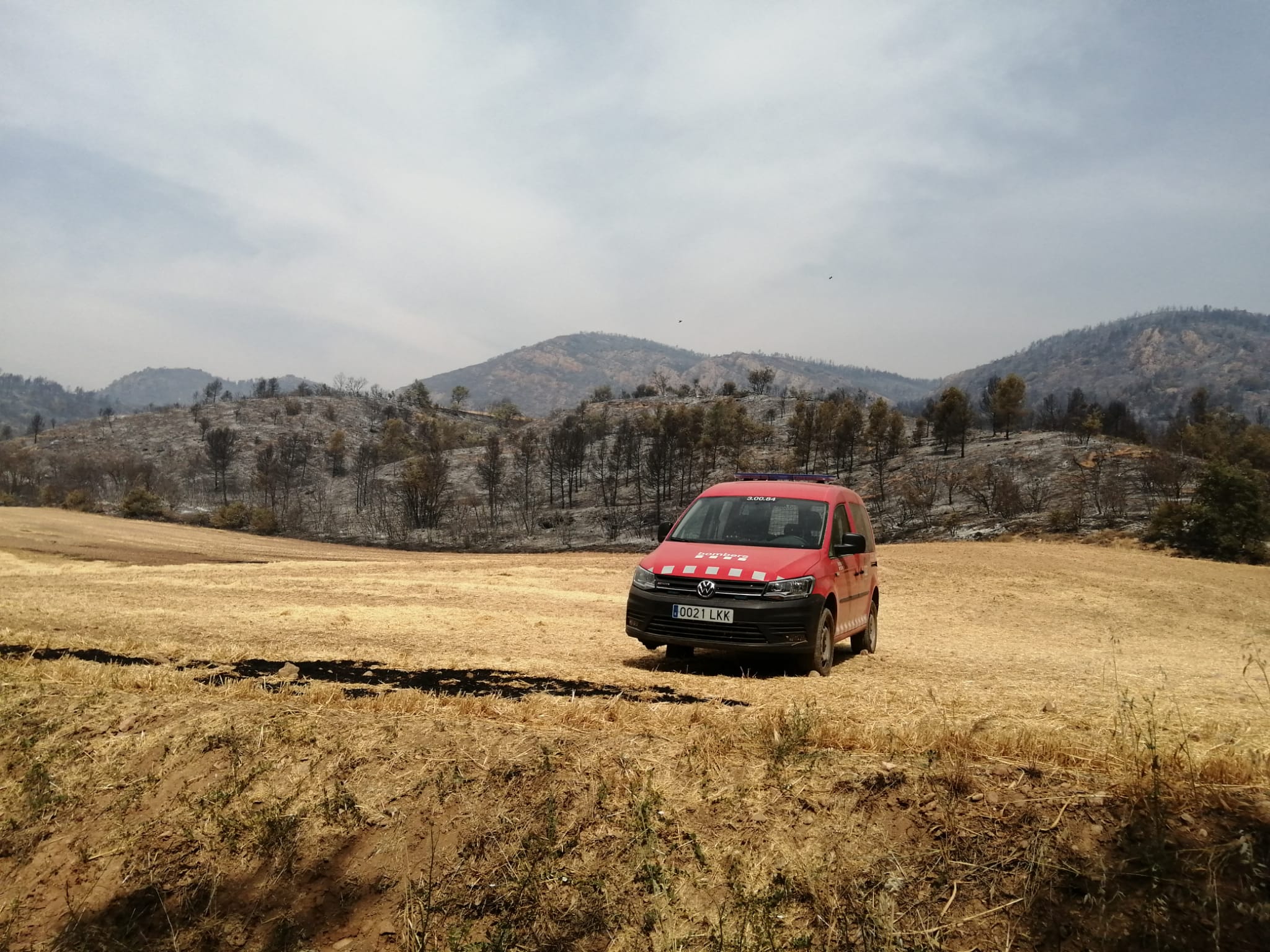Un cotxe dels Bombers, sense la roda del davant, en un camp de cereals segat, just a peu de l'incendi, en el trajecte per la carretera de Baldomar a Clua el dijous 16 de juny