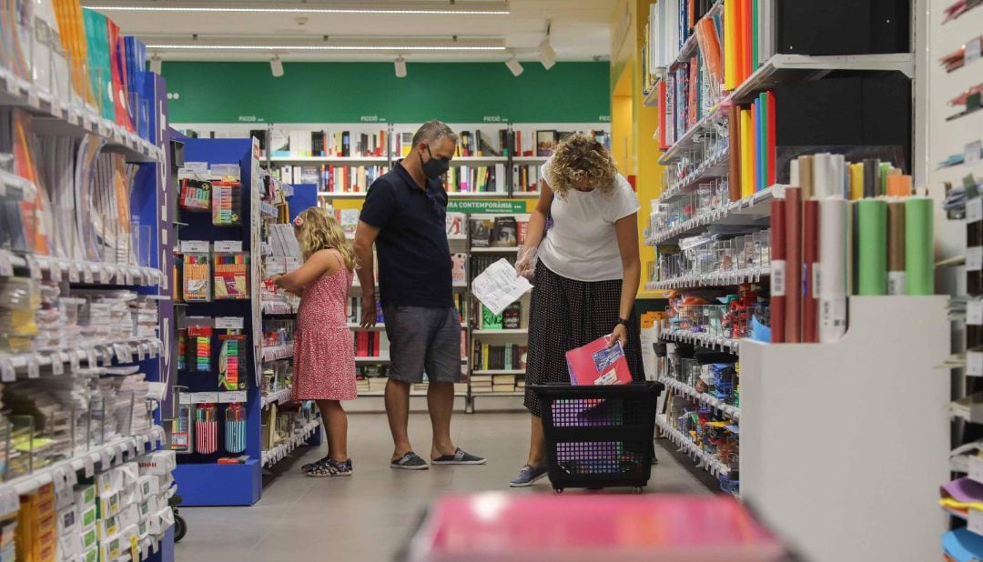 Una pareja acompañados por una niña realizan una compra de material escolar en una papelería de Valéncia.