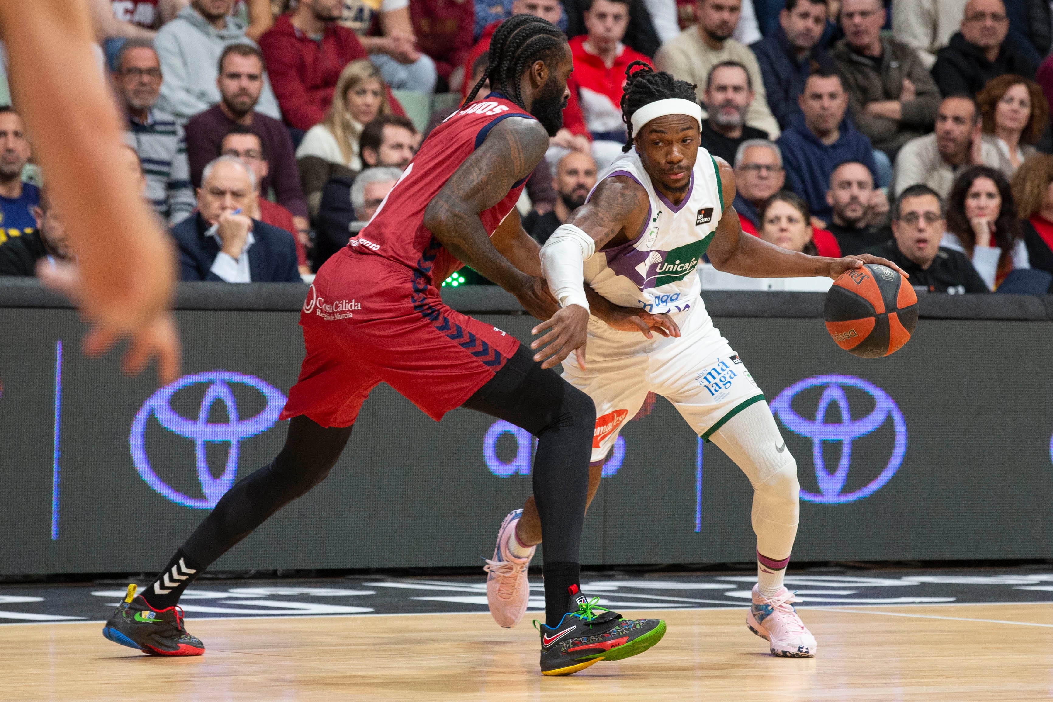 MURCIA, 22/12/2023.- El base montenegrino de Unicaja Kendrick Perry (d) controla el balón ante la presión del alero cubano de UCAM Murcia Howard Sant-Roos (i), durante el partido de la décimo quinta jornada Liga Endesa, que están disputando este viernes en el Palacio de los Deportes de Murcia. EFE/Marcial Guillén
