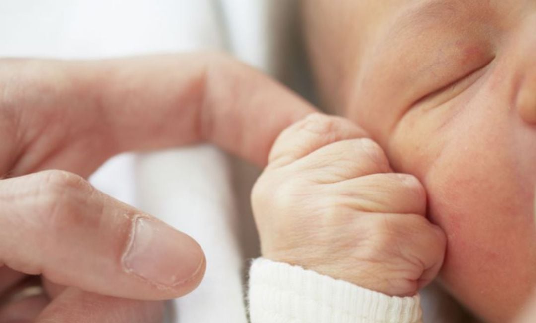 Un recién nacido se agarra al dedo de un adulto