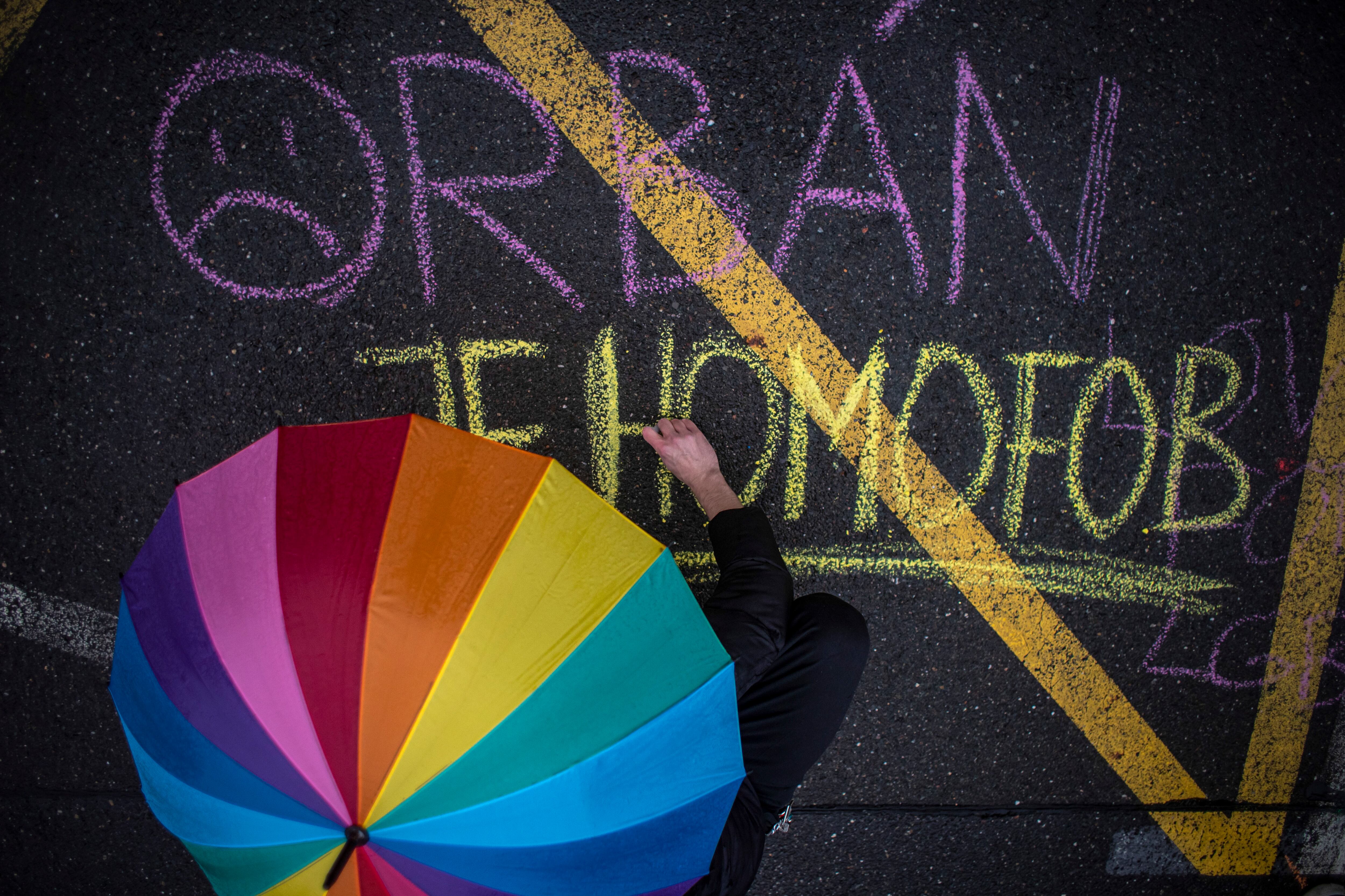 Prague (Czech Republic), 30/03/2022.- A man holds a rainbow umbrella as he writes &#039;Orban is homophobe&#039; during a protest in support of the Hungarian LGBT community in front of Hungarian embassy, in Prague, Czech Republic, 30 March 2022. Hungarian general elections is taking place same day as the government referendum about LGBT topics, on 03 April 2022. (Elecciones, Protestas, República Checa, Hungría, Praga) EFE/EPA/MARTIN DIVISEK
