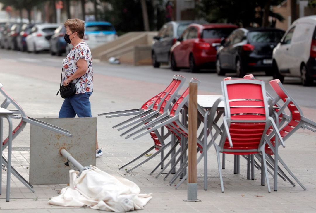 Una mujer pasa junto a una terraza recogida y afectada por le viento en València