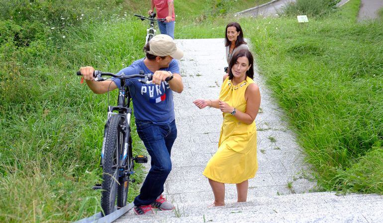 La alcaldesa comprueba cómo un vecino sube la bicicleta por la canaleta instalada.