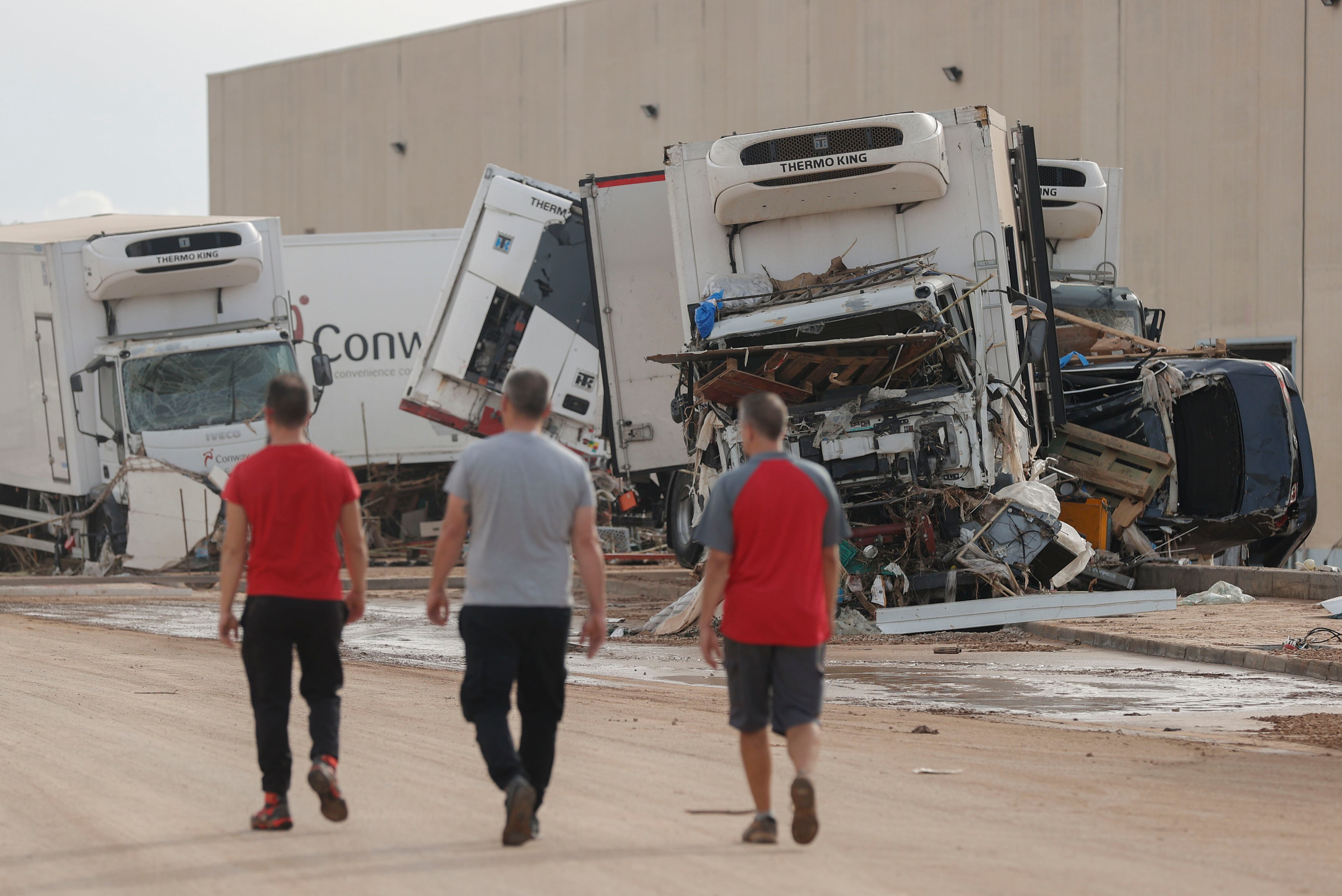 Tres hombres caminan junto a camiones destrozados en el polígono industrial de Riba-roja de Túria, este viernes