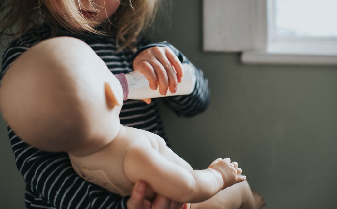 Una niña dando de beber a un bebé.