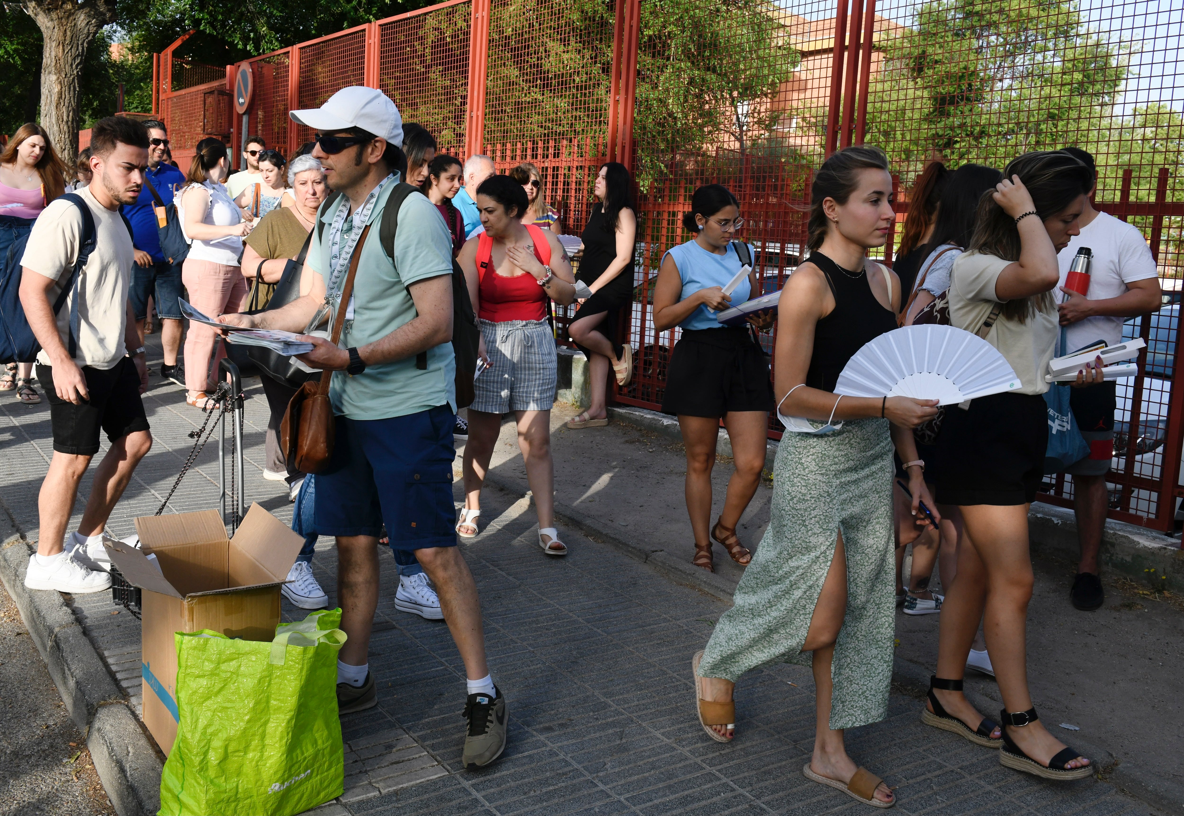 MADRID, 18/06/2022.- Varios aspirantes esperan para examinarse en el IES Butarque en Leganés, este sábado, mientras un miembro del CSIF, sindicato mayoritario en la Administración Pública, reparte información y abanicos. Más de 25.700 aspirantes a maestro se examinan en 99 sedes ubicadas en centros educativos de la región. EFE/Víctor Lerena
