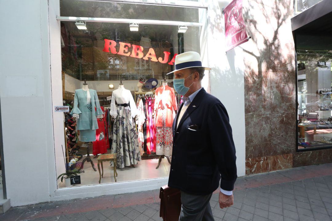 Un hombre protegido con mascarilla pasa junto a una tienda de ropa