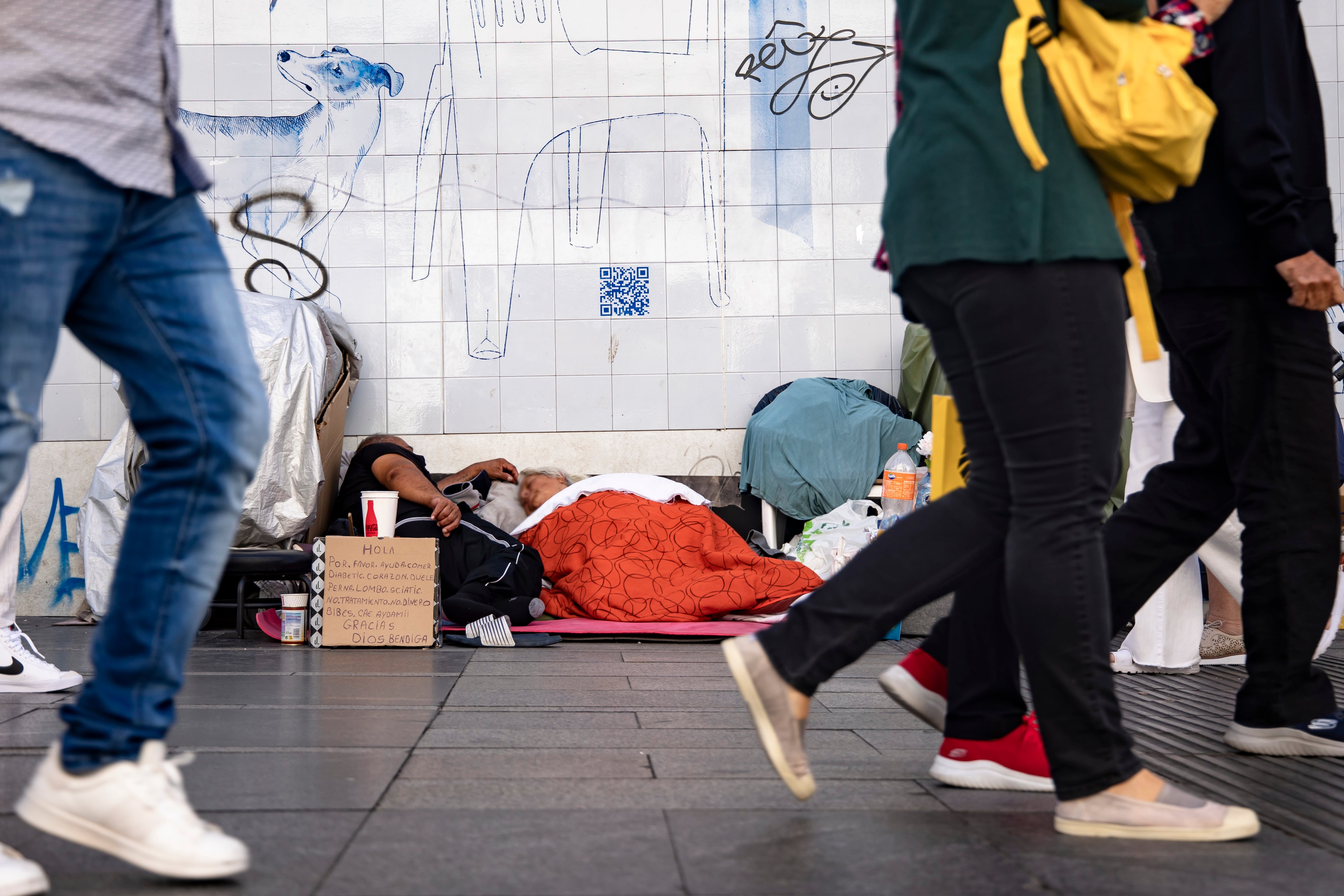 El contraste de la ciudad de Madrid: varias personas pasean por la Gran Vía mientras personas sin hogar duermen en plena calle