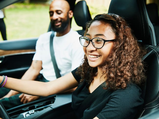 Smiling young woman in drivers seat of car while taking driving lesson from father
