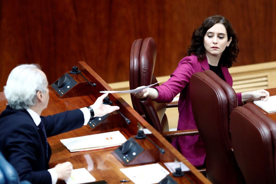 La presidenta de la Comunidad de Madrid, Isabel Díaz Ayuso  le entrega un papel al consejero de Sanidad, Enrique Ruiz Escudero durante la sesión.