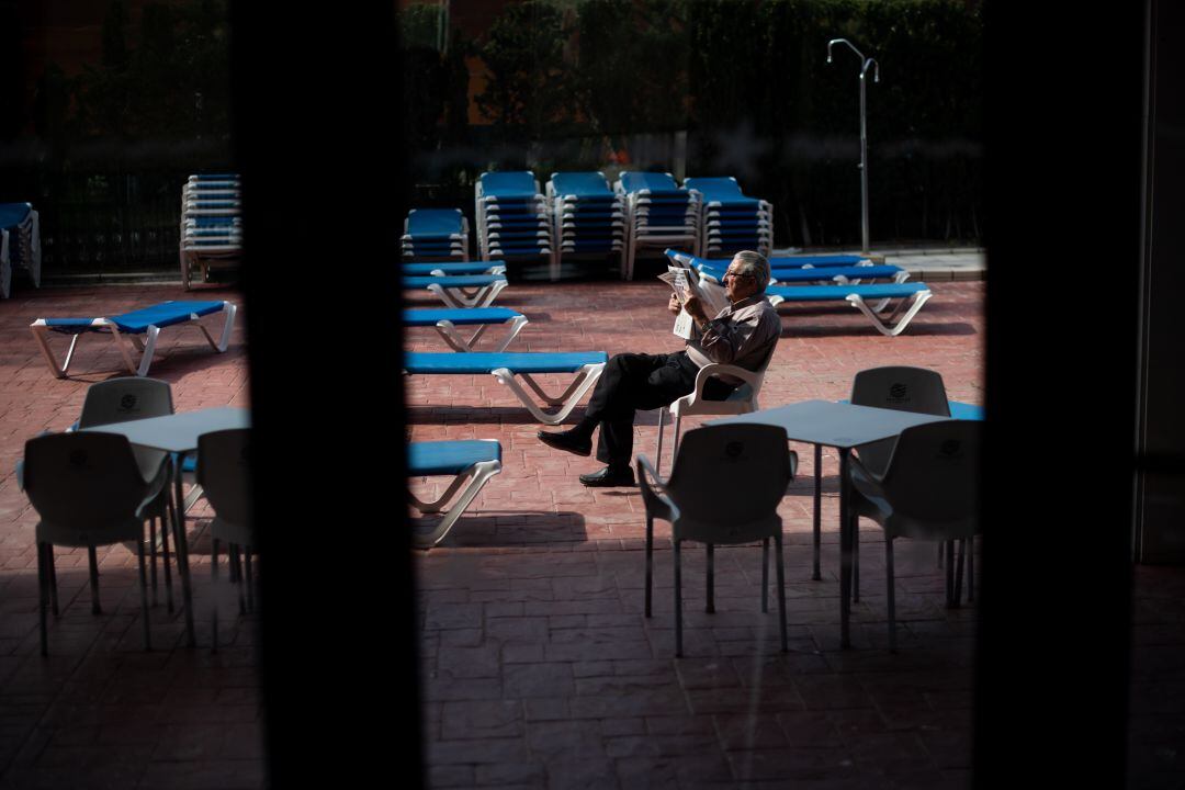 Un hombre lee el periódico en el recinto de la piscina de un  hotel