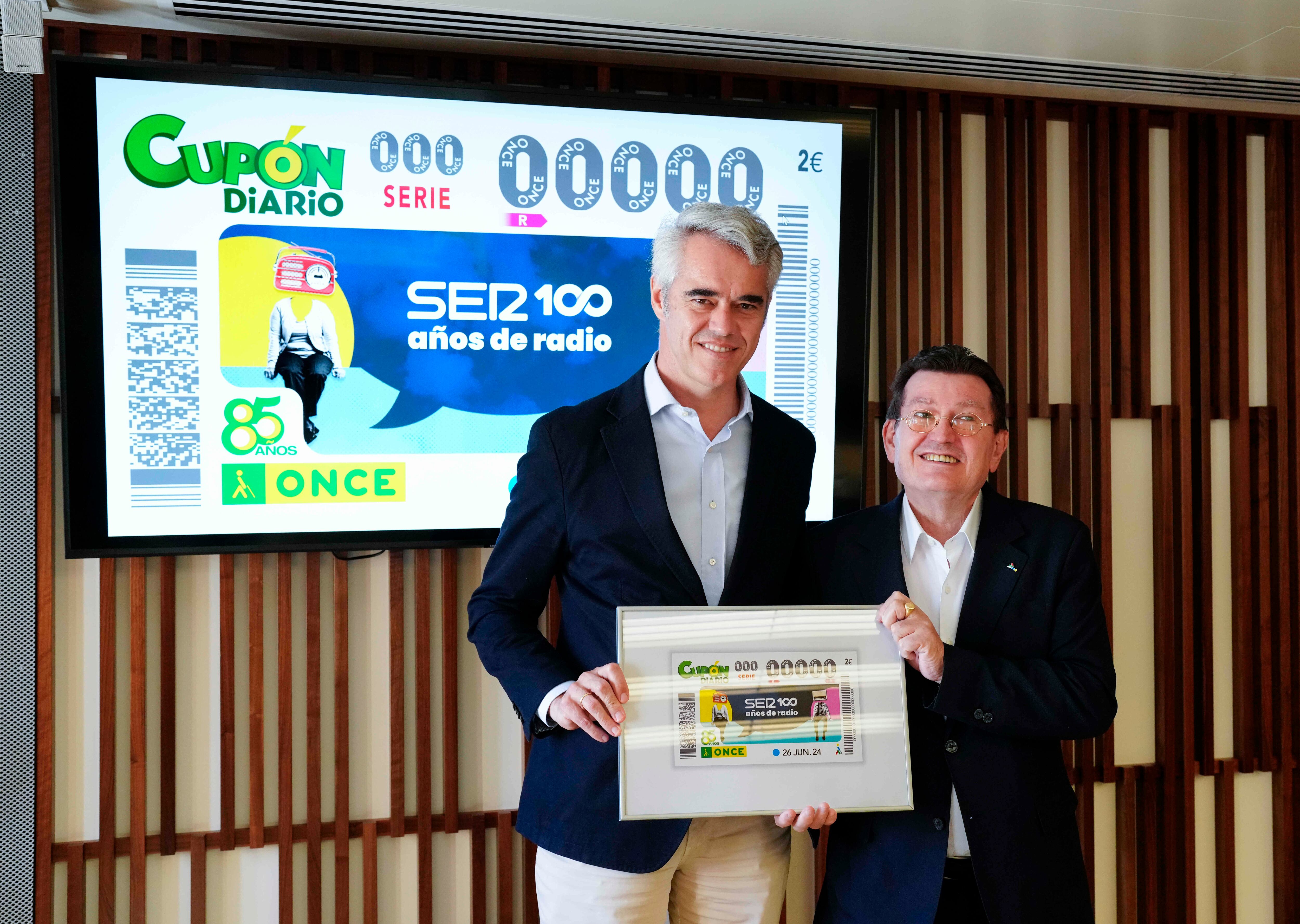 Ignacio Soto, director general de la SER, y Ángel Sánchez, director general de la ONCE, sostienen una lámina enmarcada con el cupón del centenario de la radio