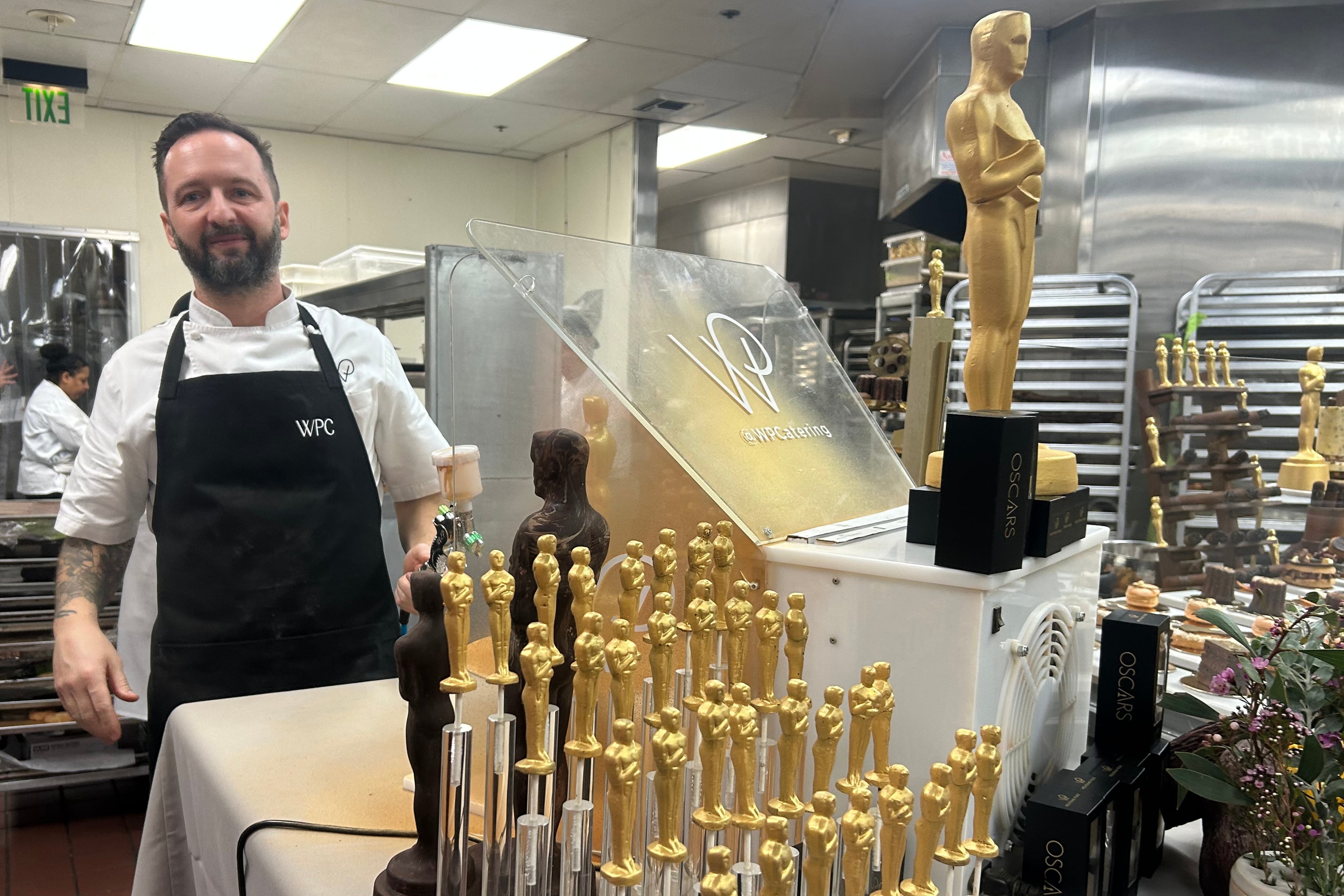 Un ayudante de cocina posa junto a figuras de chocolate de la estatuilla de los premios Oscar.