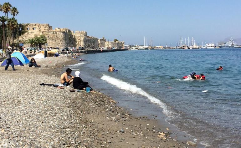 Refugiados aprovechan los chalecos salvavidas que van quedando de centenares de travesías previas para bañarse y librarse del calor