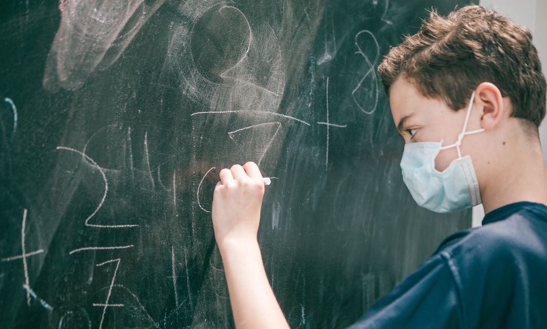 Un joven hace una operación matemática en la pizarra.