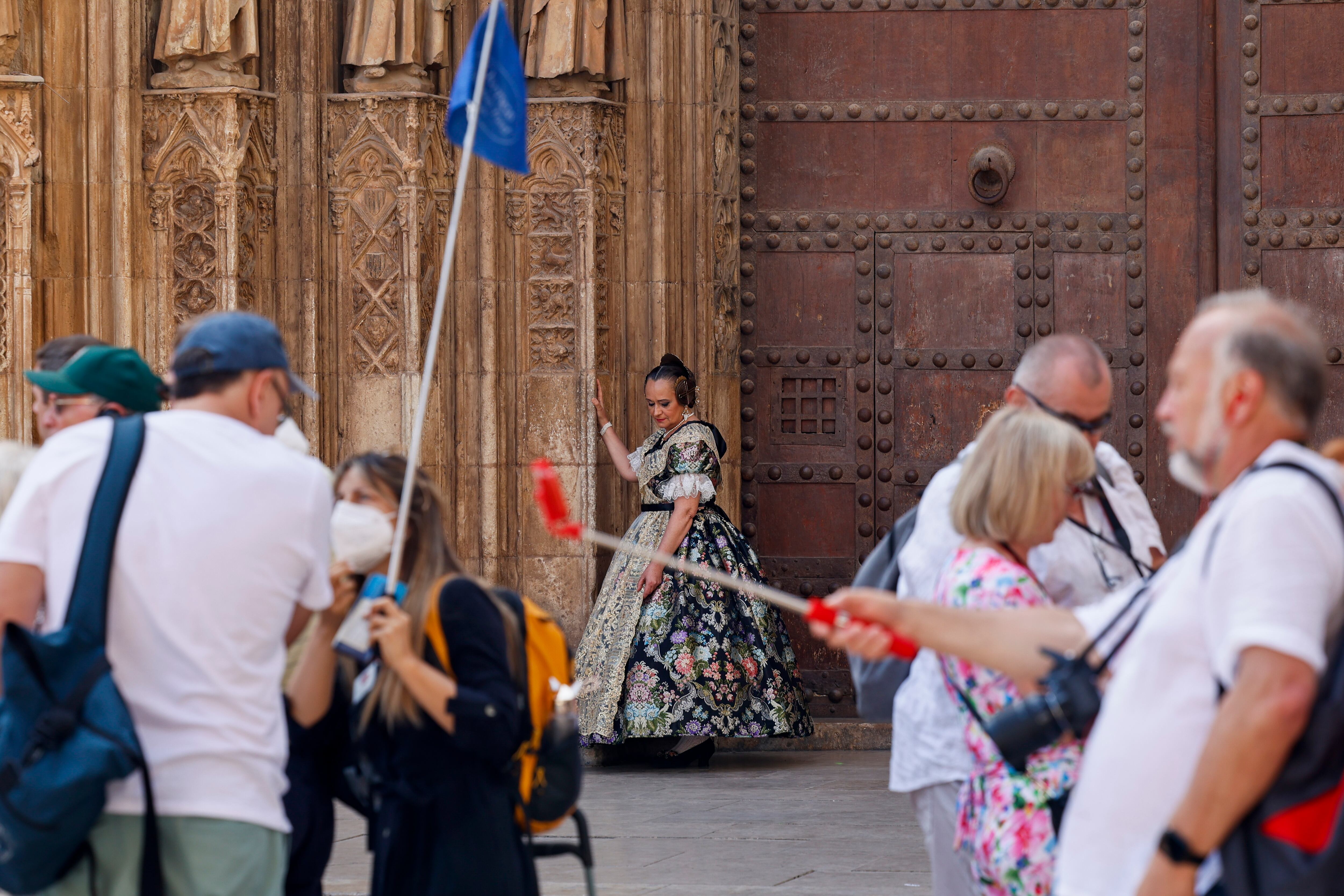 Un grupo de turistas pasea junto a la catedral de Valencia en presencia de una fallera que descansa en la puerta de los Apóstoles del edificio durante este viernes en el que se siguen viviendo temperaturas veraniegas.