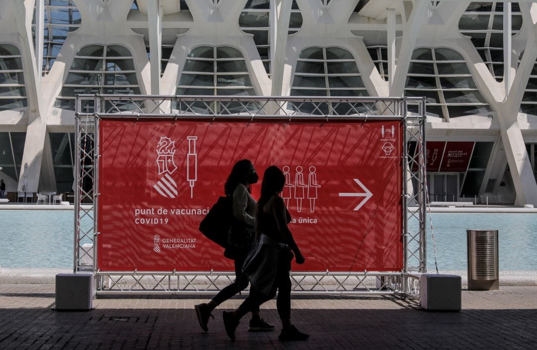 Dos personas pasan por un cartel que indica el punto de vacunación de la Ciudad de las Artes y las Ciencias de València. 